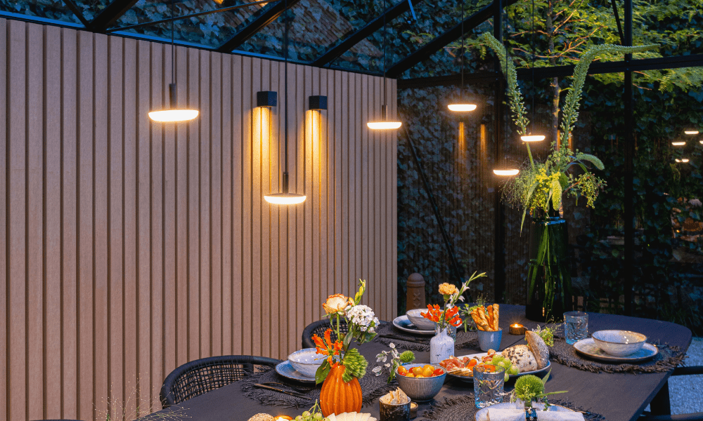Ein ansprechend gedeckter Gartentisch in einem &uuml;berdachten Au&szlig;enbereich wird von sechs Outdoor-H&auml;ngelampen beleuchtet, die in unterschiedlicher H&ouml;he verspielt aufgeh&auml;ngt wurden. An der Wand h&auml;ngen zwei passende Au&szlig;enwandleuchten.