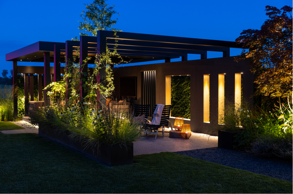 Eine Pergola wird von Aufbau-Deckenleuchten und Bodenspots von in-lite beleuchtet, sodass das Ger&uuml;st bei Nacht effektvoll hervortritt.
